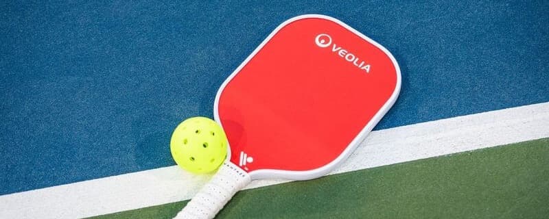 Red pickleball paddle with Veolia sponsorship laying on a pickleball court