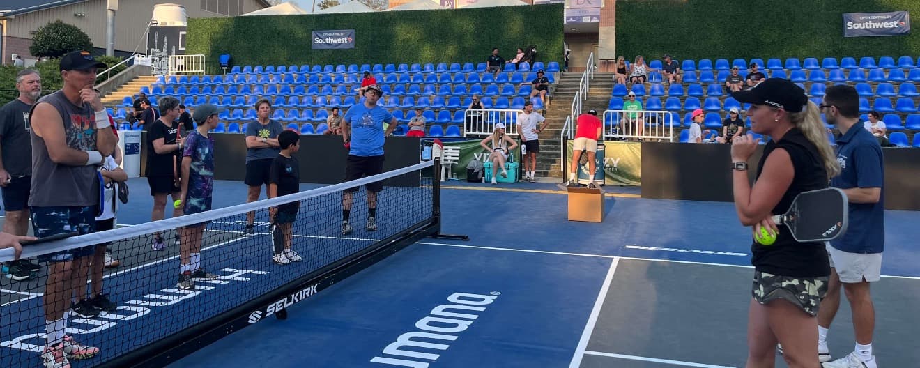 Brooke Buckner standing on one side of the pickleball court, talking to a group of amateur players