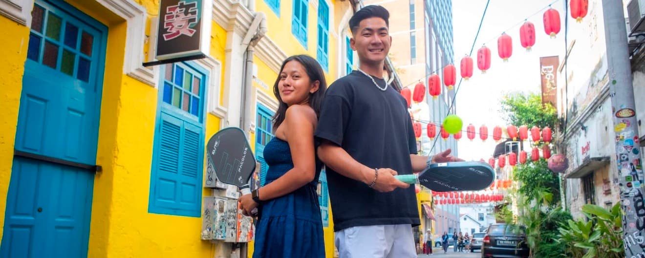 Jimmy Liong and Mia Athilla posing on a street with pickleball paddles.